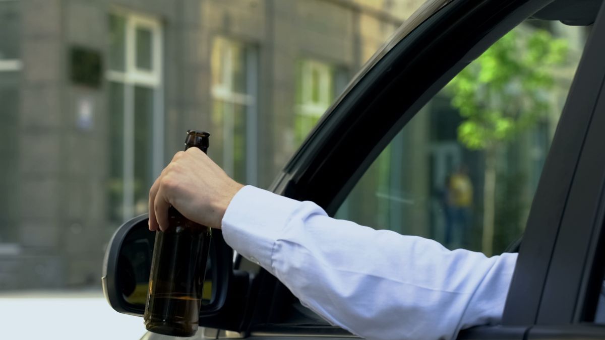 Man holding beer bottle inside car, drinking alcohol while driving, crash risk