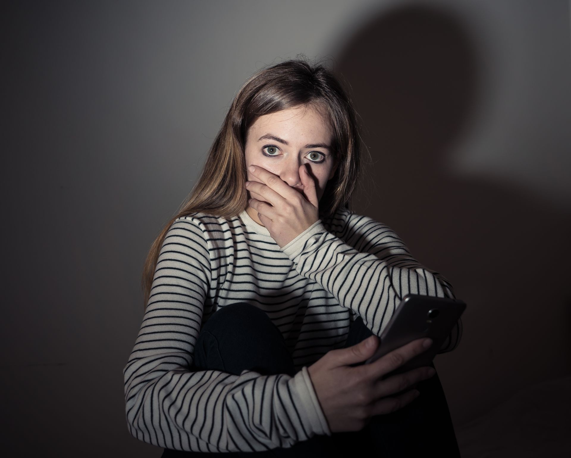 Sad desperate young teenager female girl on smart phone suffering from online bulling and harassment felling lonely and hopeless sitting on bed at night. CYberbullying and dangers of internet concept.
